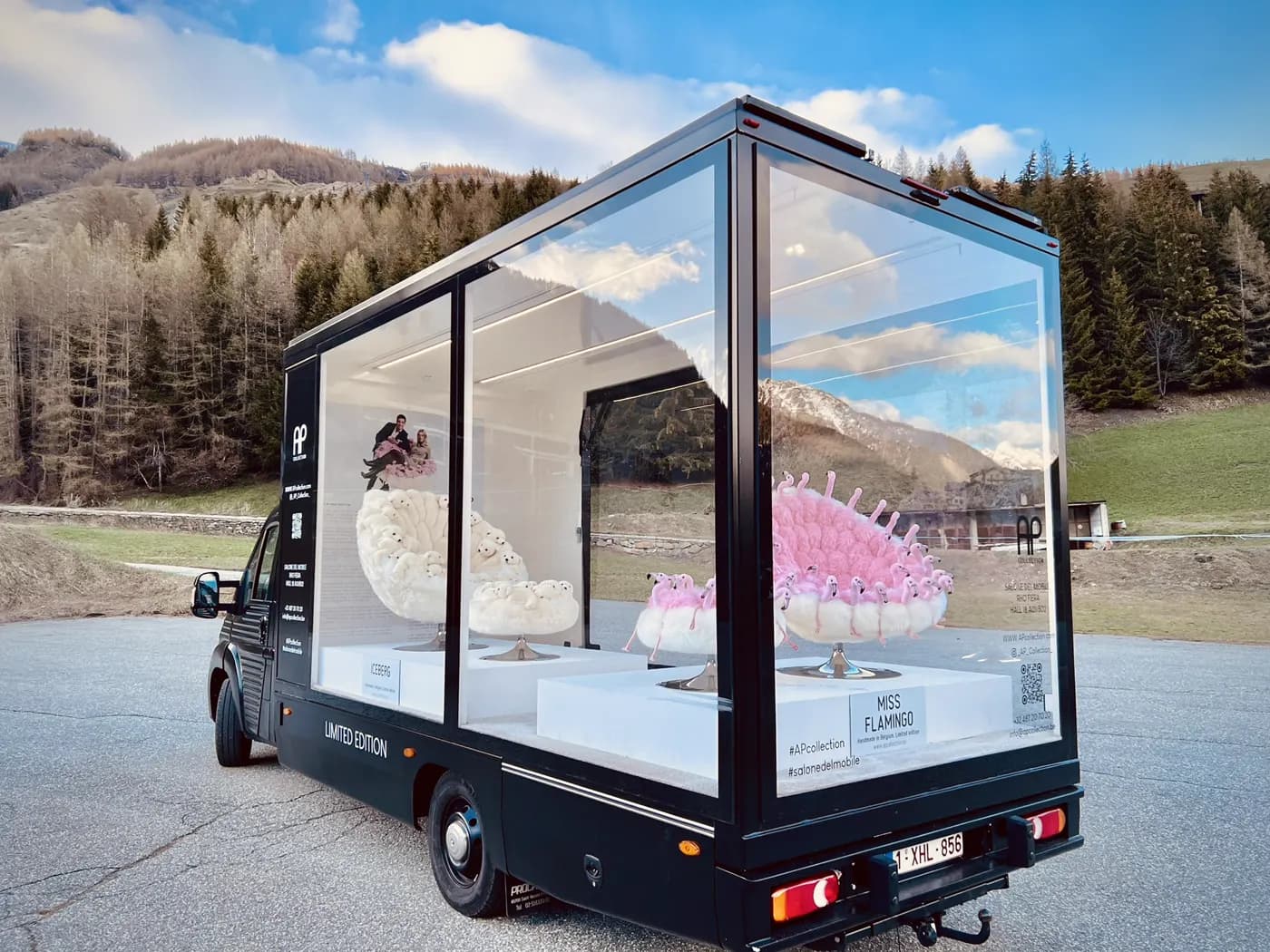 Camion vitrine transparent exposant deux fauteuils design sur socles éclairés, décor de montagne