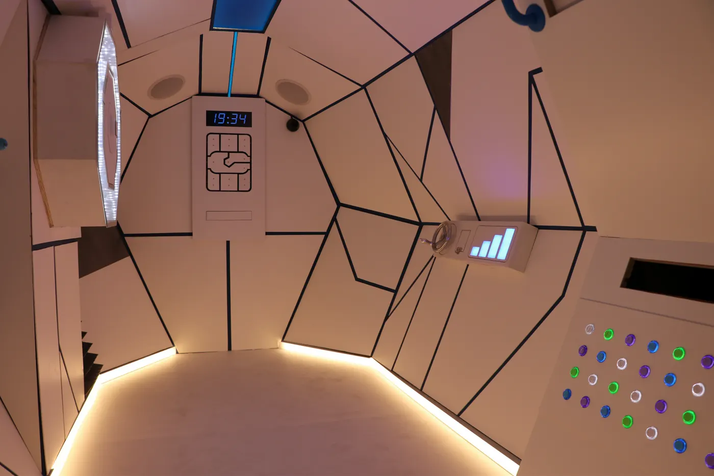 Intérieur d'une caravane transformée en escape game : parois à facettes, trappes et boutons lumineux