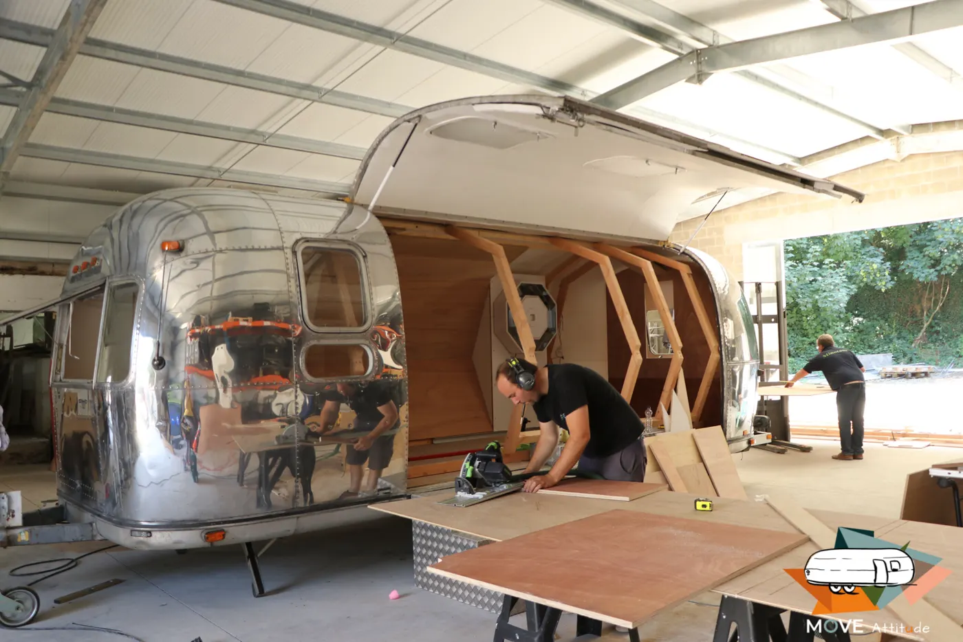 Caravane Airstream ouverte en atelier, ossature de bois à facettes et trappes octogonales en cours de montage