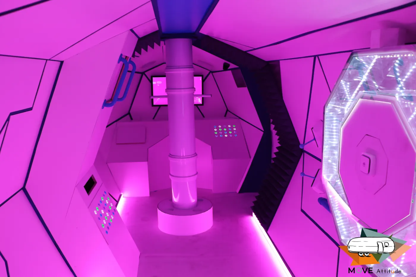 Intérieur de l'escape game éclairé en magenta, parois à facettes et commandes lumineuses