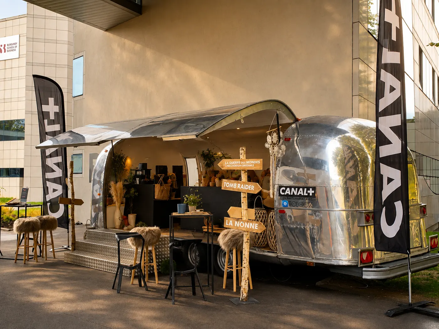 Caravane Airstream chromée ouverte en bar, panneaux directionnels en bois et beach flags de la chaîne