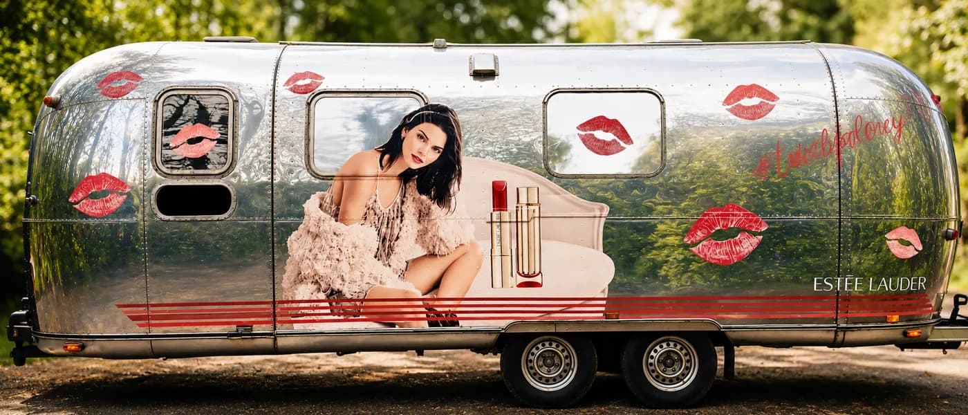 Caravane chromée habillée d'empreintes de bouche rouges, garée sous les arbres