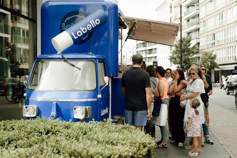 Le triporteur ouvert en rue piétonne, file de passants le long d'une haie taillée