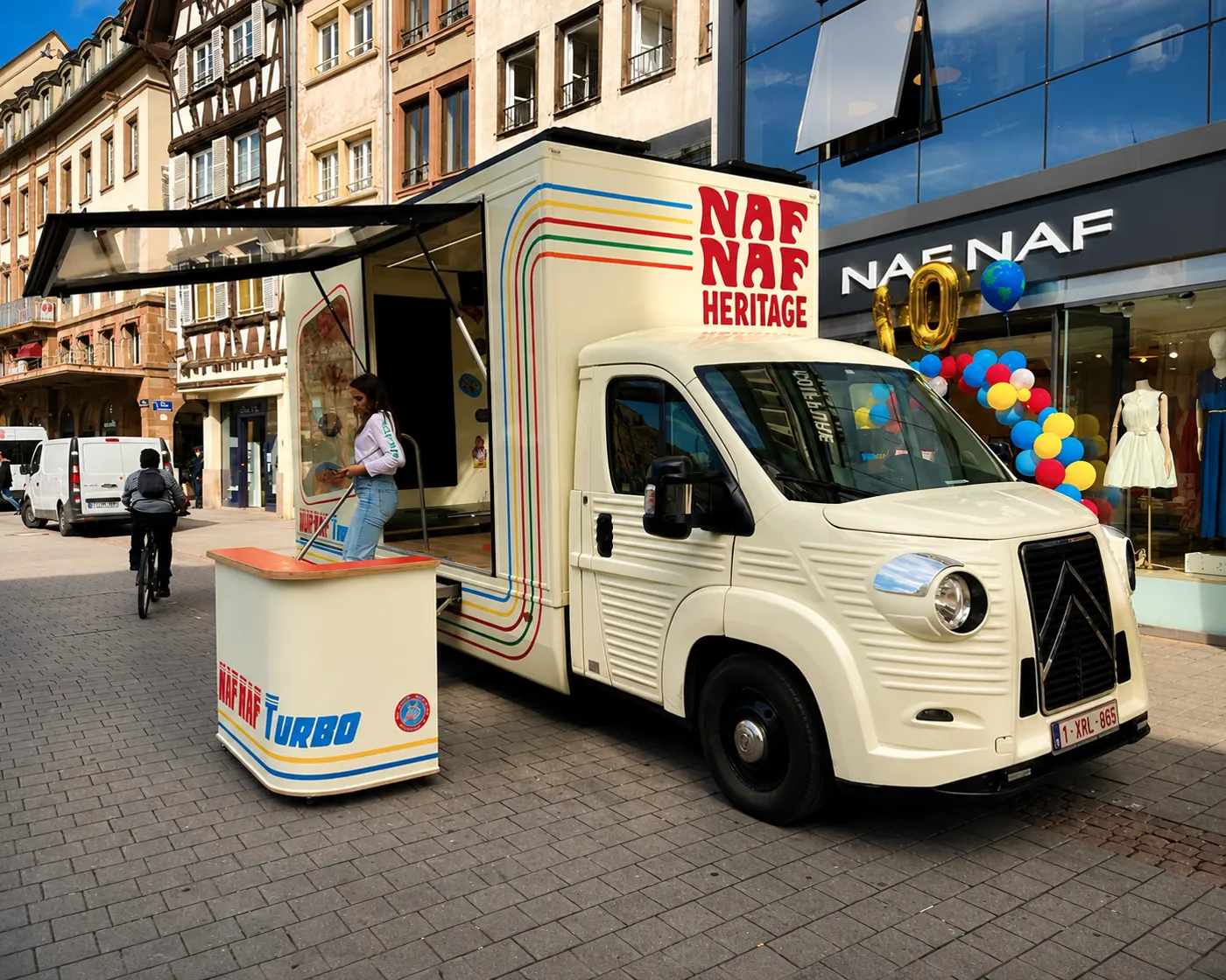 Camion boutique habillé « NAF NAF Heritage » stationné devant la vitrine de l'enseigne, ballons colorés et comptoir installé