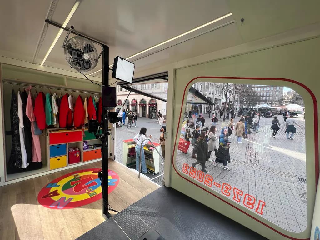Intérieur d'un camion boutique : portants de vêtements, casiers colorés et tapis rond, flanc ouvert sur la rue