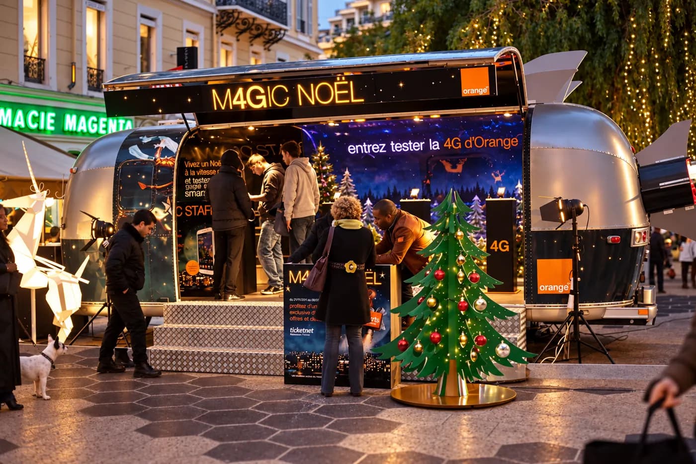 Caravane « Magic Noël » ouverte au crépuscule, visiteurs devant l'entrée et sapin lumineux