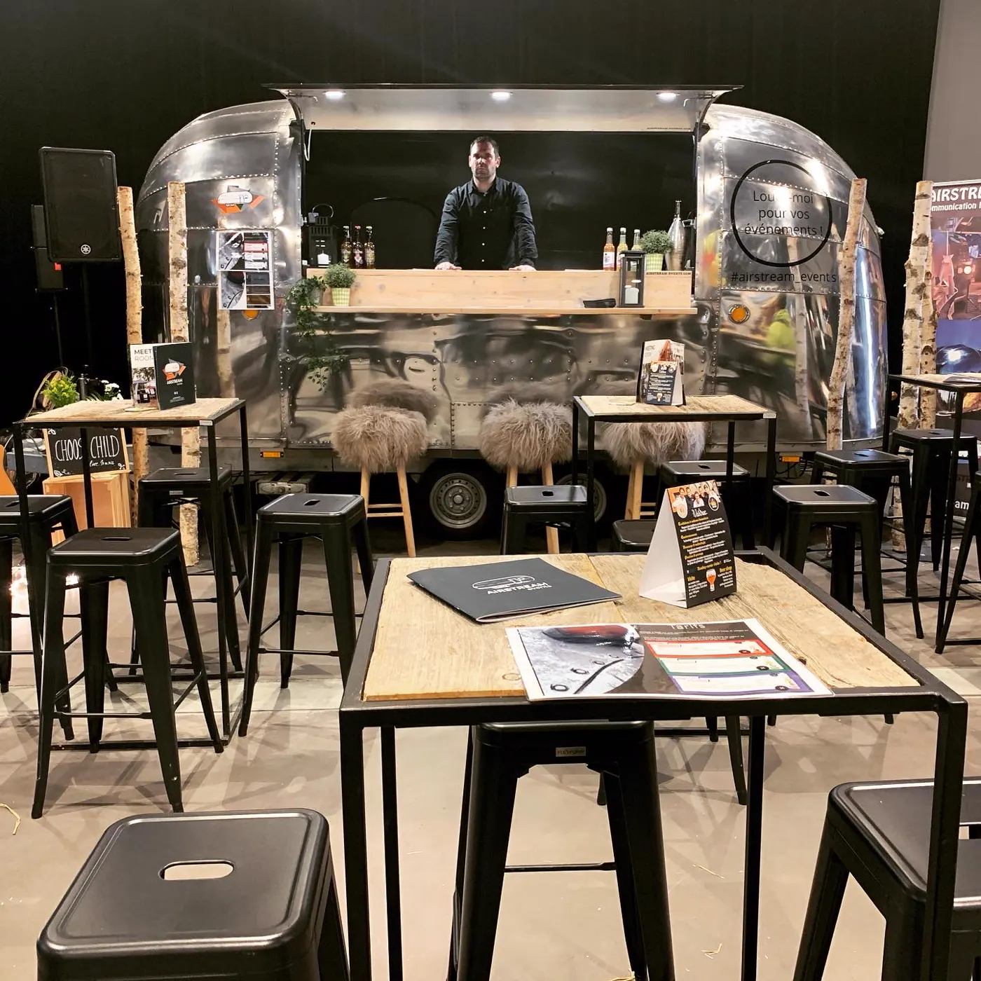 Caravane Airstream aménagée en bar dans une salle, mange-debout et tabourets hauts