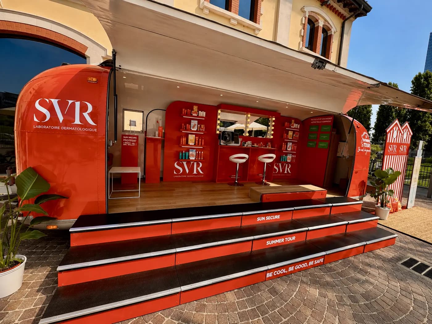 Caravane habillée de rouge, ouverte sur toute sa longueur en boutique de soins avec tabourets hauts