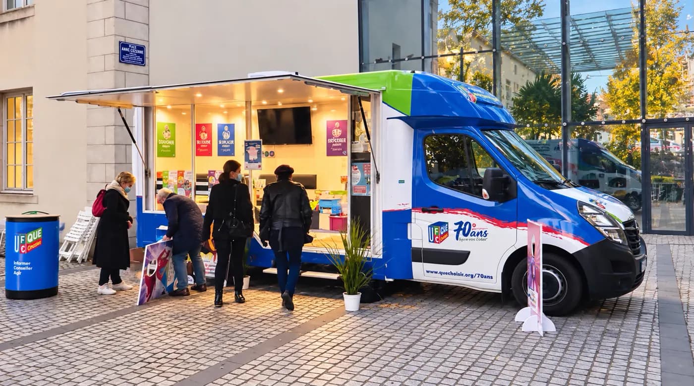 Camion Infotruck ouvert sur une place pavée, visiteurs devant le comptoir d'accueil éclairé