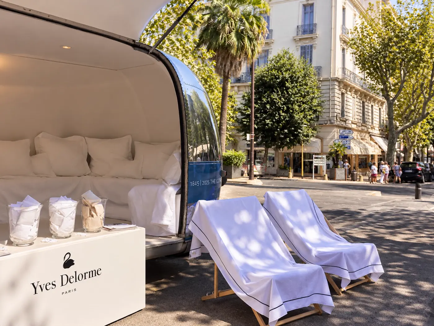 Lit dressé de linge blanc dans la caravane ouverte, présentoir de la marque au premier plan