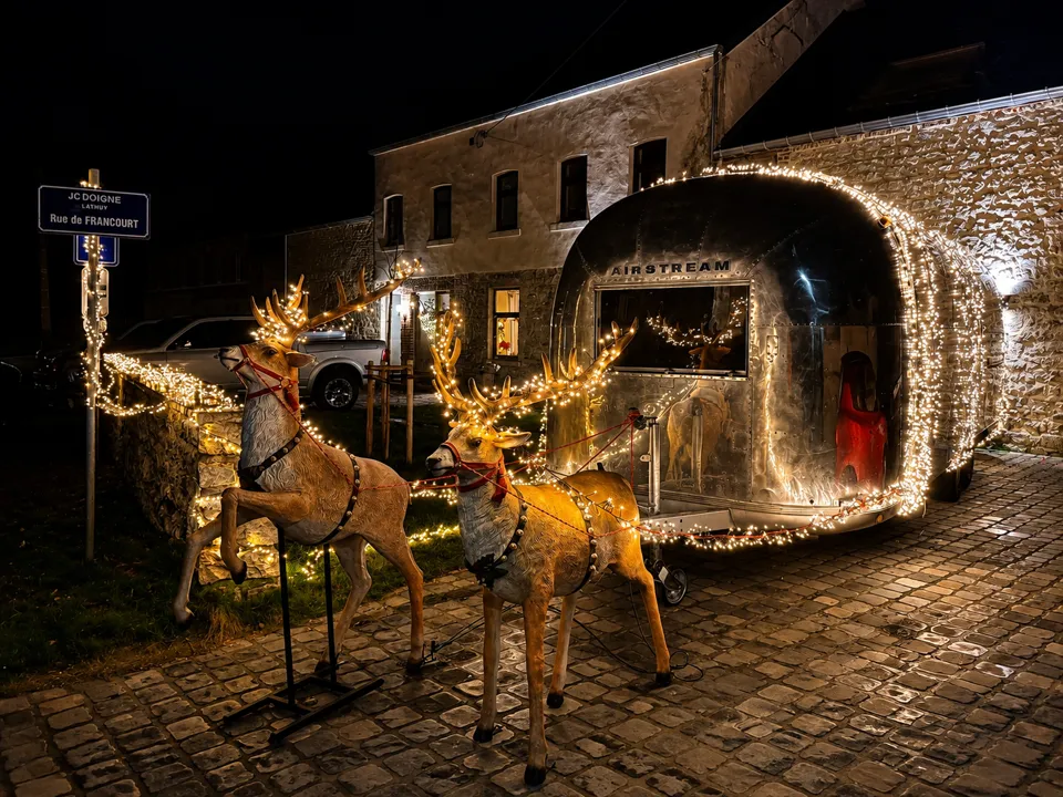 Caravane Airstream couverte de guirlandes lumineuses, rennes lumineux au premier plan, de nuit sur des pavés